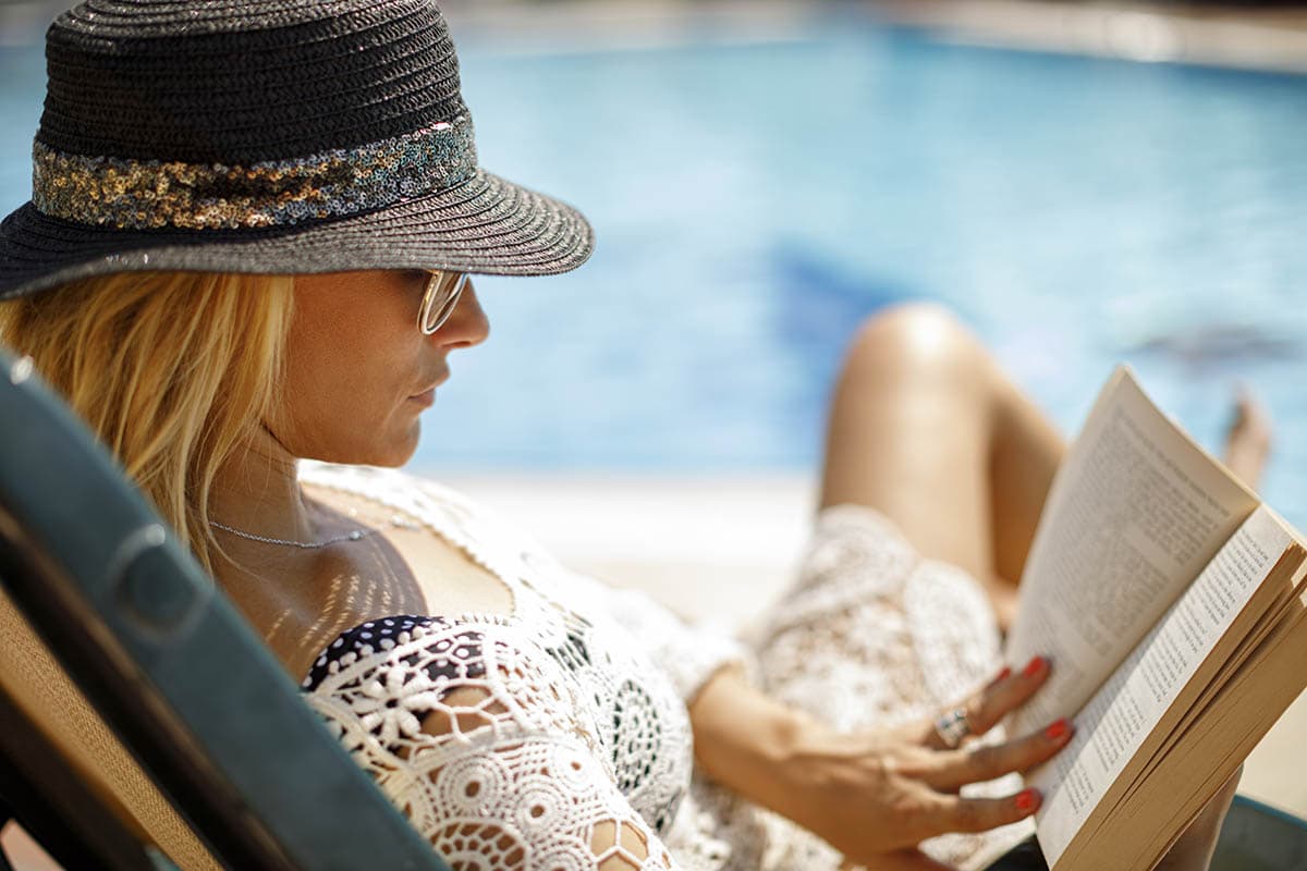 Woman relaxing beside her pool reading a book