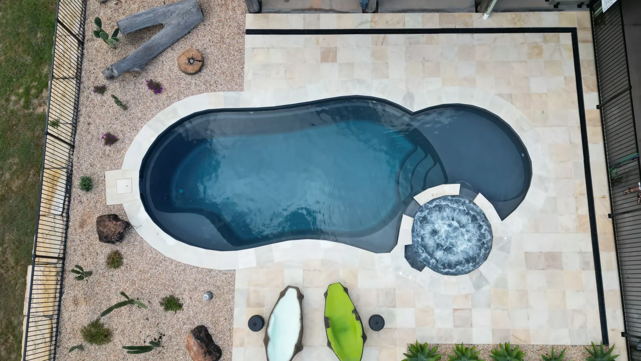 The Allure 9.10m fibreglass swimming pool is installed in a modern house with white tiles and pool accessories surrounding it. The beautiful Graphite Grey pool colour stands out from the grey-themed house, accented by green and white surfboards.