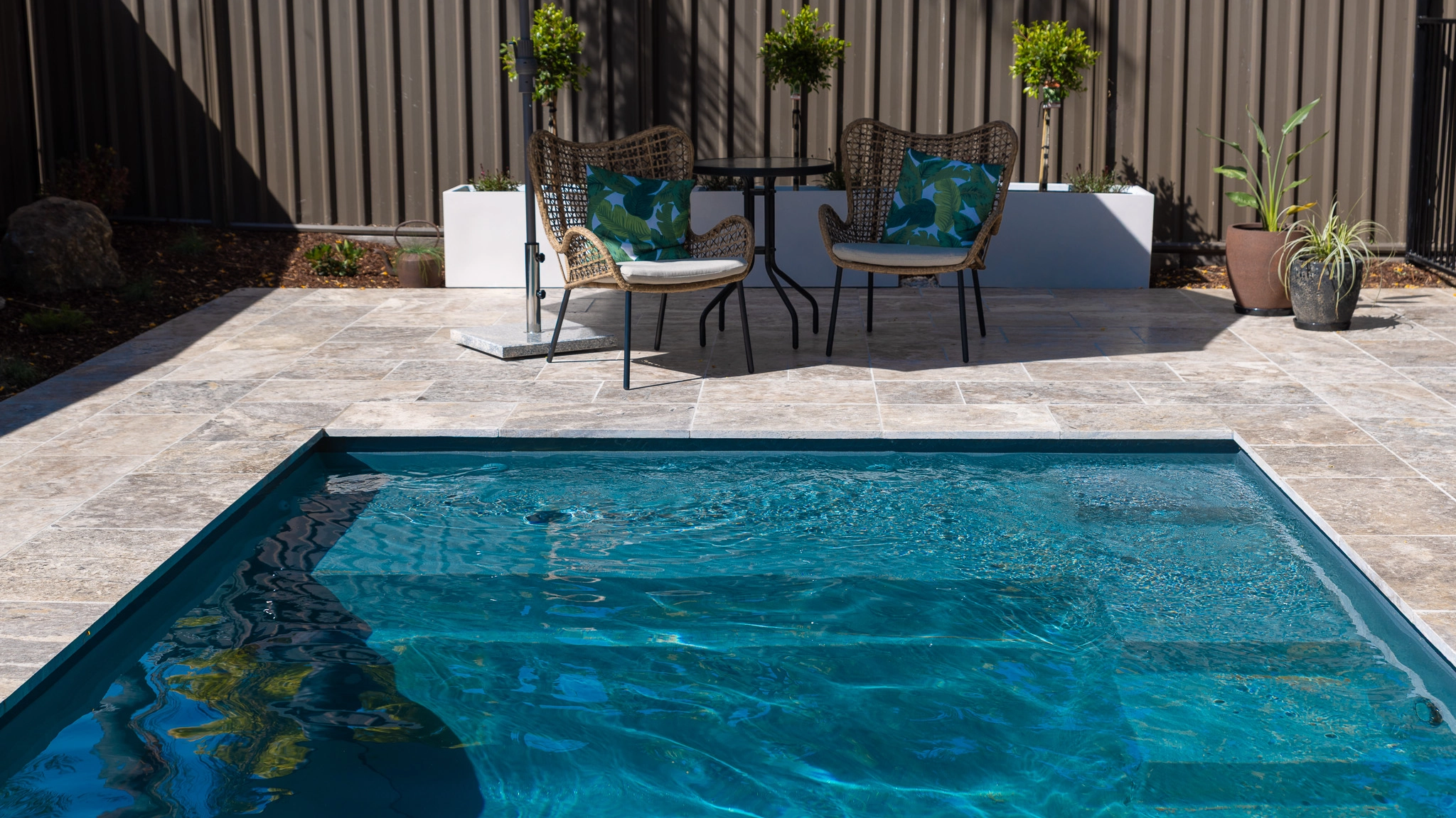 The Precision 6.00m fibreglass swimming pool is installed in front of a white countryside farmhouse, with greenery and mountains surrounding it. The mysterious Graphite Grey gives a modern look to the overall countryside aesthetics.