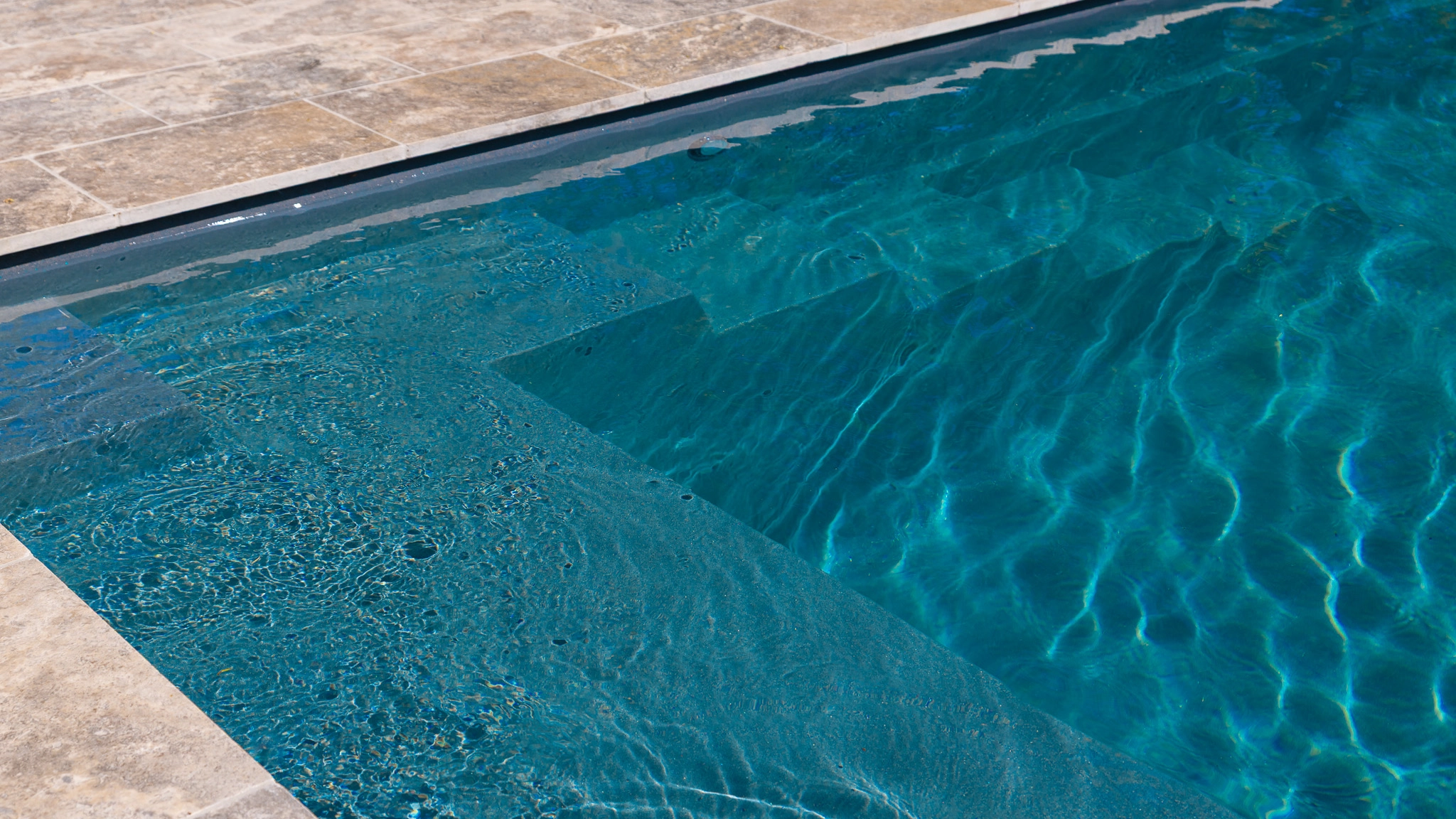 The Precision 6.00m fibreglass swimming pool is installed in front of a white countryside farmhouse, with greenery and mountains surrounding it. The mysterious Graphite Grey gives a modern look to the overall countryside aesthetics.