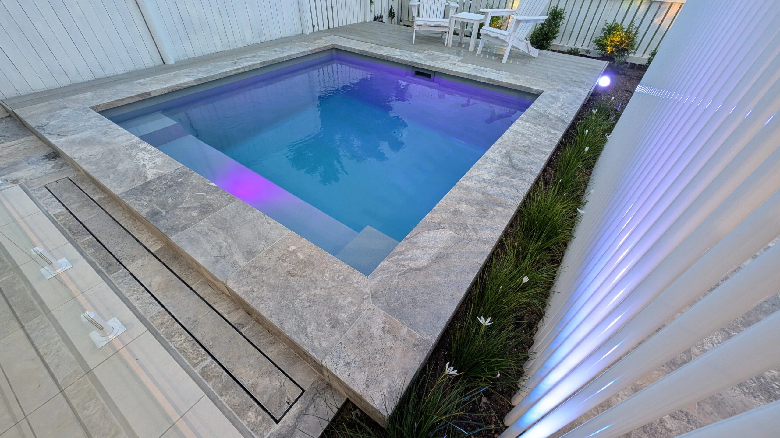 The Platinum Plunge 3.50m fibreglass swimming pool is installed in a modern house with white tiles and pool accessories surrounding it. The beautiful Silver Grey pool colour matches perfectly with the grey dusk sky.