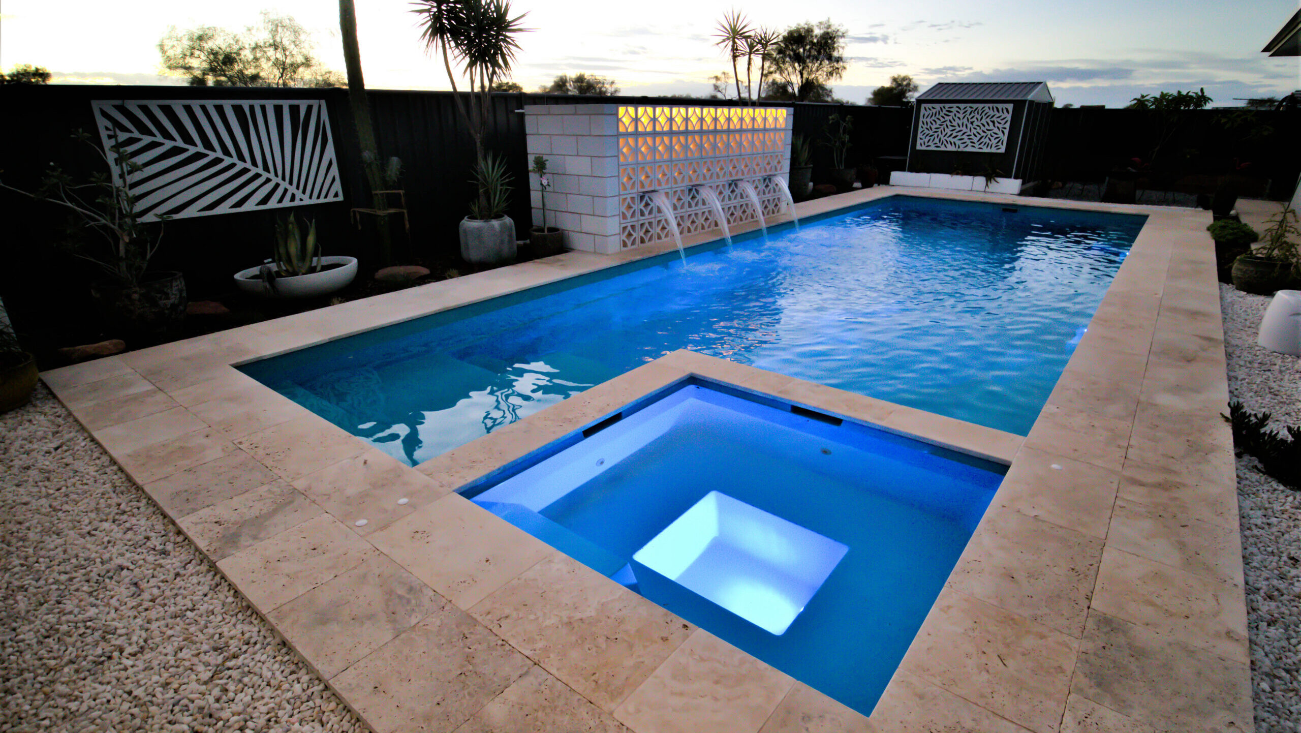 The Absolute 12.00m fibreglass swimming pool with a built-in spa is built at the heart of a contemporary design complex with white tiles surrounding it. The pool and built-in spa come in Crystal Blue colour, while the house is in yellow and brown.