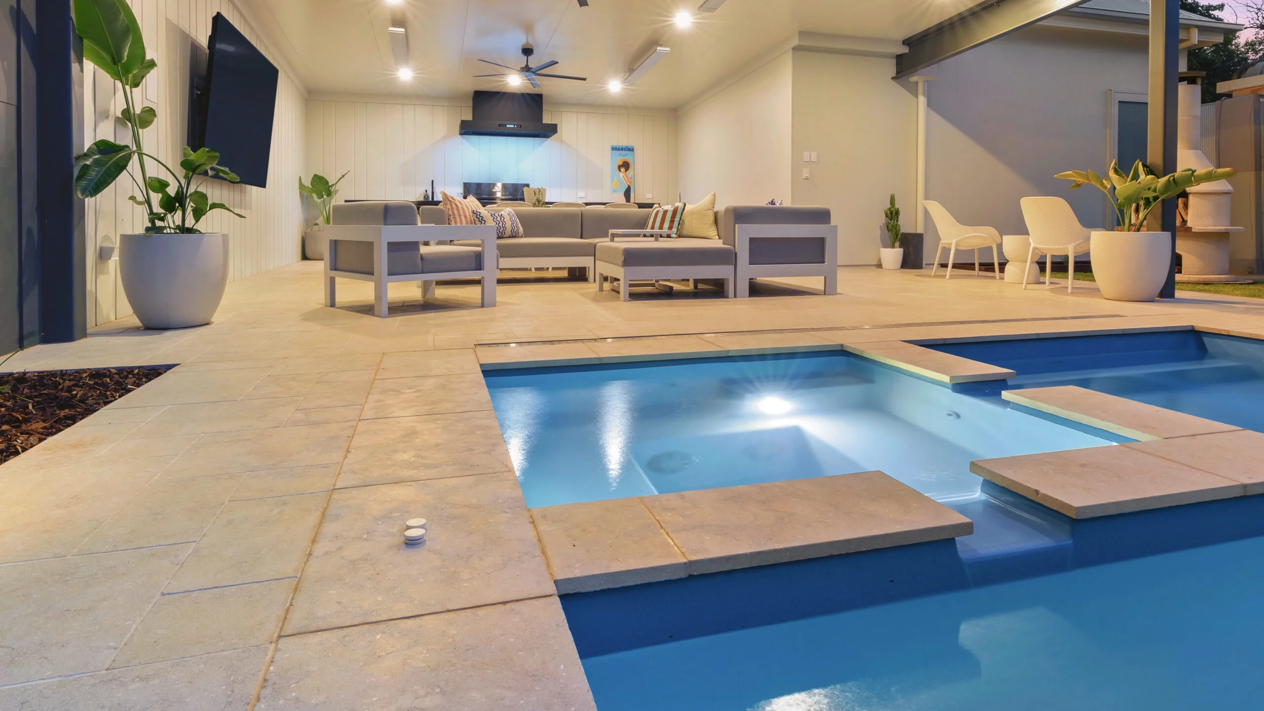 The Absolute 12.00m fibreglass swimming pool is installed in the heart of a heritage house with a pool house next to it and palm trees in the background. Its stunning Silver Grey colour stands out from the white heritage house with dim lighting at dawn.
