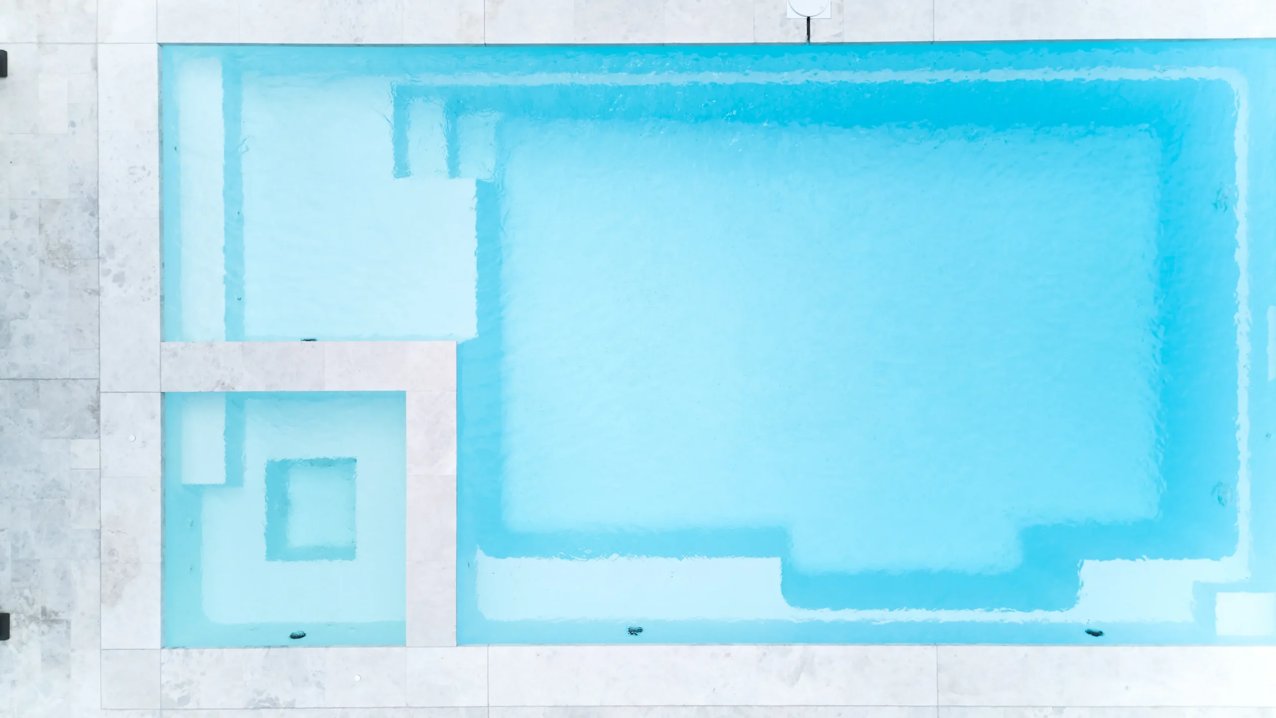 The Absolute 8.00m fibreglass swimming pool in Shimmer White is installed in a landscaped backyard in Rye, Mornington Peninsula, Victoria. The pool is surrounded by light stone paving, frameless glass fencing, manicured hedges and a shaded outdoor seating area. The Shimmer White finish creates bright, pale blue water that complements the neutral paving and lush greenery, creating a fresh and inviting space for family swimming and relaxation.