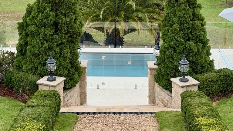 The Precision 8.05m fibreglass swimming pool is installed in front of a large white countryside mansion, with greenery and mountains surrounding it. The mysterious Graphite Grey gives a modern look to the overall countryside aesthetics.