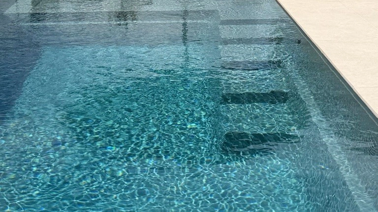 The Precision 8.05m fibreglass swimming pool is installed in front of a large white countryside mansion, with greenery and mountains surrounding it. The mysterious Graphite Grey gives a modern look to the overall countryside aesthetics.