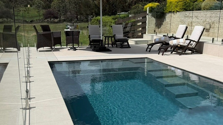 The Precision 8.05m fibreglass swimming pool is installed in front of a large white countryside mansion, with greenery and mountains surrounding it. The mysterious Graphite Grey gives a modern look to the overall countryside aesthetics.