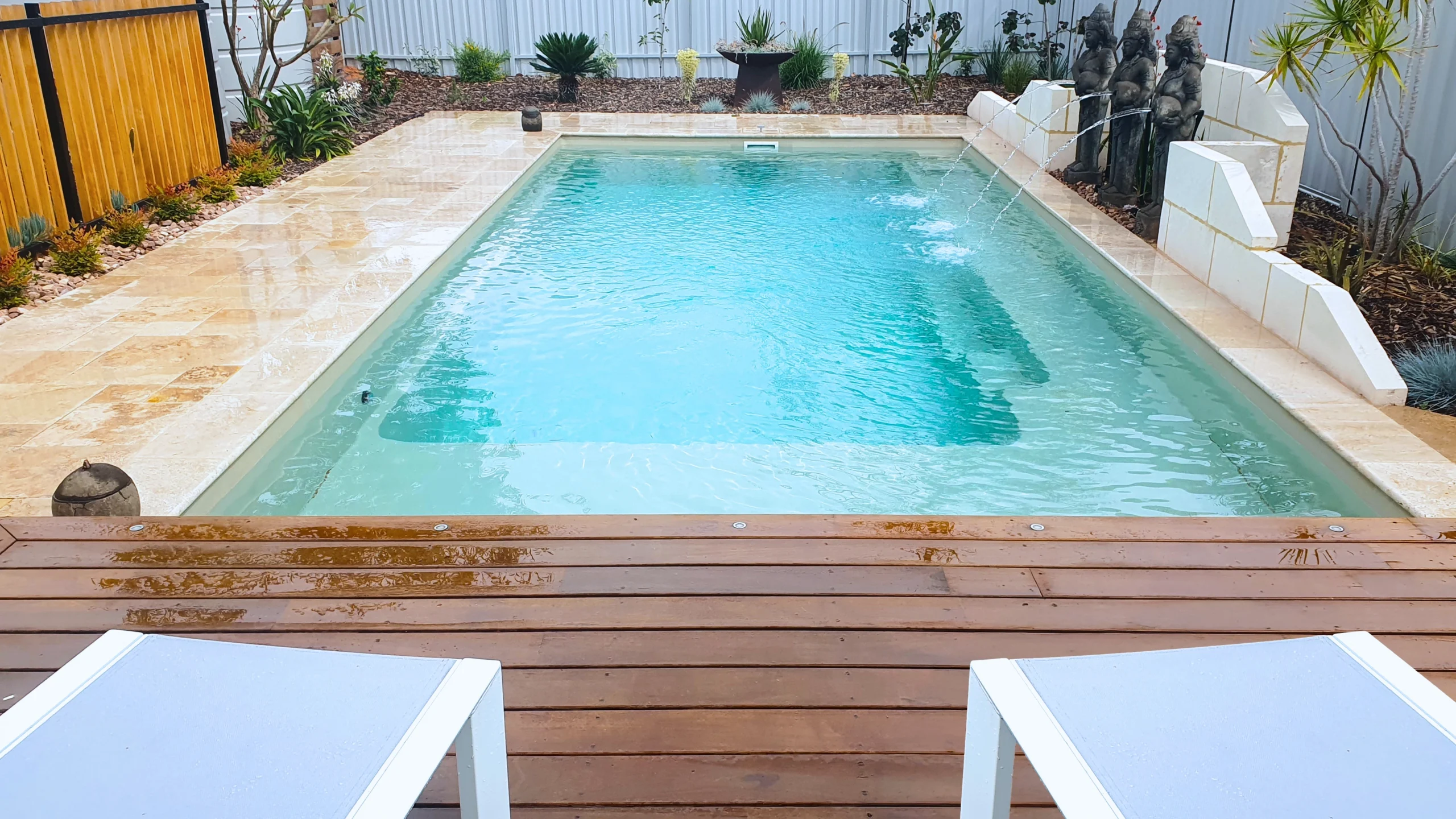 The Reflection with Splash Deck 8.50m fibreglass swimming pool in Diamond Sand is installed in a landscaped backyard in Barmera, South Australia. The pool is surrounded by light beige stone paving, warm timber decking, decorative water features and lush greenery. The Diamond Sand finish creates a soft blue-green water colour that complements the natural tones of the paving and timber, creating a tranquil and inviting outdoor retreat.