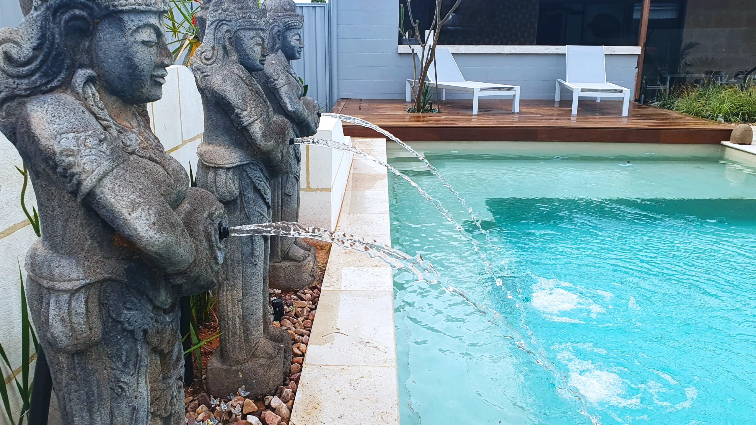The Reflection with Splash Deck 8.50m fibreglass swimming pool in Diamond Sand is installed in a landscaped backyard in Barmera, South Australia. The pool is surrounded by light beige stone paving, warm timber decking, decorative water features and lush greenery. The Diamond Sand finish creates a soft blue-green water colour that complements the natural tones of the paving and timber, creating a tranquil and inviting outdoor retreat.