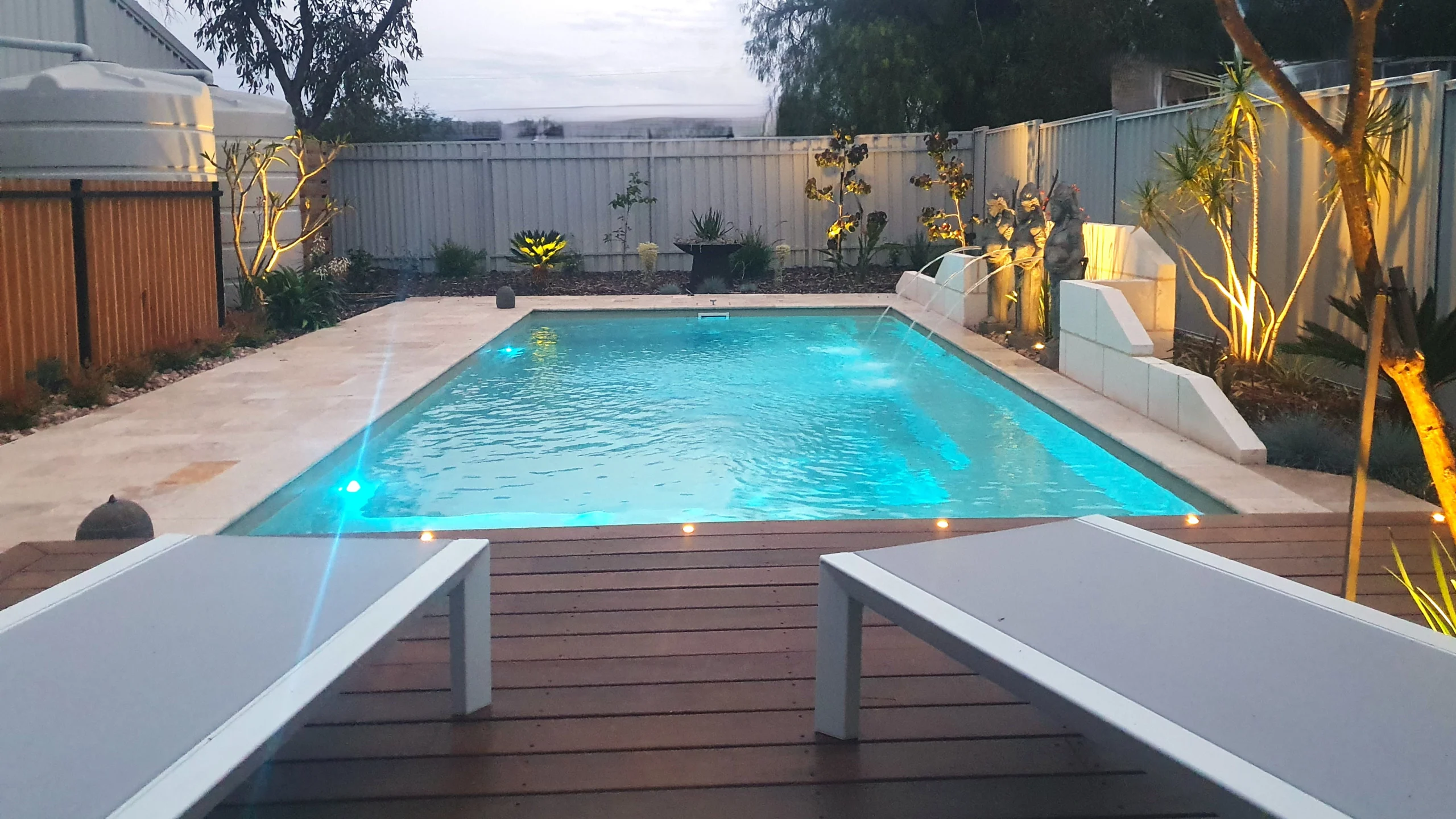 The Reflection with Splash Deck 8.50m fibreglass swimming pool in Diamond Sand is installed in a landscaped backyard in Barmera, South Australia. The pool is surrounded by light beige stone paving, warm timber decking, decorative water features and lush greenery. The Diamond Sand finish creates a soft blue-green water colour that complements the natural tones of the paving and timber, creating a tranquil and inviting outdoor retreat.
