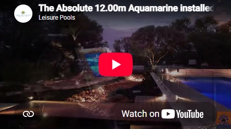 The Absolute 12.00m fibreglass swimming pool with a built-in spa is in the middle of the backyard, with red tiles and greenery surrounding it. The pool colour is aquamarine makes the fibreglass swimming pool stand out from the mountainous background and dawn sky.